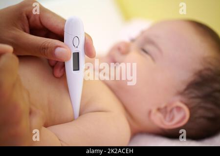 Vermeidung von Fieber. Ein süßes Mädchen, das lacht, während ihre Mutter ihre Temperatur unter den Arm nimmt. Stockfoto