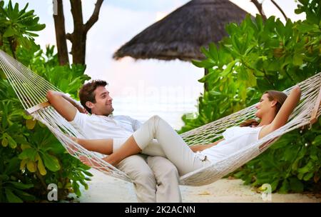 Entspannung und Romantik - UrlaubenKurzurlaube. Aufnahme eines glücklichen Paares, das sich in einer Hängematte in ihrem eigenen privaten Paradies entspannt - Romantik. Stockfoto