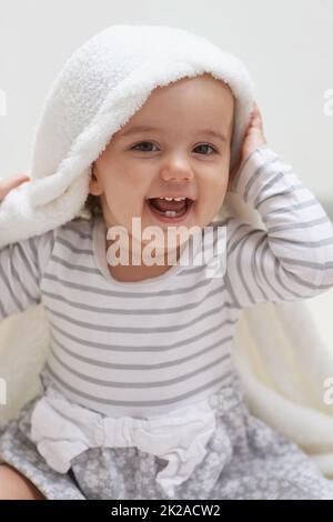 Guck-a-boo. Aufnahme eines niedlichen kleinen Mädchens, das auf dem Boden sitzt und mit ihrer Decke spielt. Stockfoto