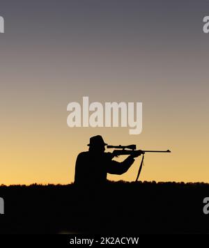 Aufnahme wird vorbereitet. Eine Silhouette eines Mannes im Freien, der sein Scharfschützengewehr hochhält. Stockfoto