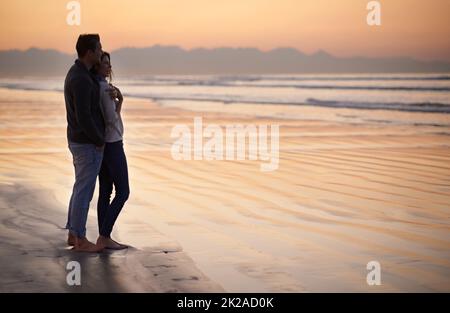 Es gibt nichts wie junge Liebe. Silhouette eines jungen Paares, das einen romantischen Spaziergang am Strand genießt. Stockfoto