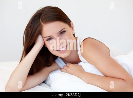 Genießen Sie das Schlafen im Urlaub. Eine wunderschöne junge Frau lächelt, während sie im Bett liegt. Stockfoto