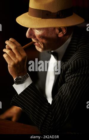 Leuchtet auf. Gealterter Mobboss, der einen Hut trägt und ernst aussieht, während er eine Zigarette anzündet. Stockfoto