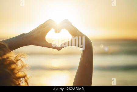 Ich muss den Sommer lieben. Nahaufnahme einer nicht identifizierbaren Frau, die mit ihren Händen am Strand eine Herzform formt. Stockfoto