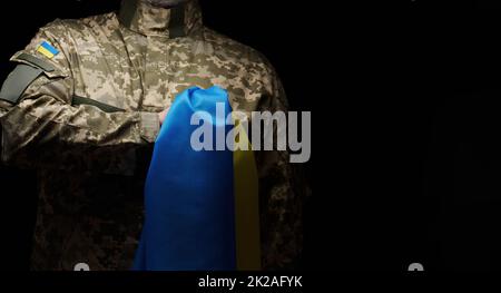 Der ukrainische Soldat hält eine Flagge des unabhängigen Staates der Ukraine. Standhaftigkeit und Mut des Volkes im Kampf gegen die Eindringlinge. Ungebrochener Geist der Nation. Symbol der Unabhängigkeit Stockfoto