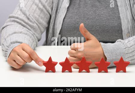 Customer Experience Feedback-Konzept. Fünf rote Sterne, die beste Bewertung für ausgezeichnete Dienstleistungen mit einer weiblichen Hand zu treffen. Weißer Tisch Stockfoto