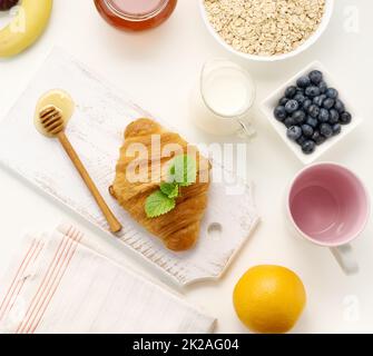 Frühstück am Morgen, rohe Haferflocken auf einem Keramikplatte, Milch im Dekanter, Heidelbeeren und Honig im Glas Stockfoto