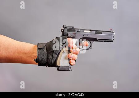 Die Hand eines Mannes hält eine schwarze Pistole in der Hand auf einem grauen Hintergrund Stockfoto