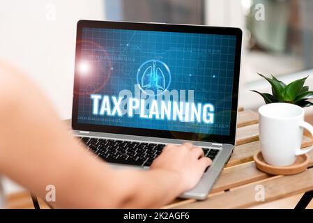 Das Schild zeigt Tax Planning an. Ein Wort über die Analyse von Finanzeinkünften und die Planung von Geschäftsbuchhaltung. Neben Coffe Tasse und Plant Working From Home auf dem Laptop tippen. Stockfoto