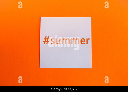 Weißes Papierquadrat auf orangefarbenem Hintergrund mit dem Hashtag Summer in englischer Sprache, prägnanter Stil Stockfoto