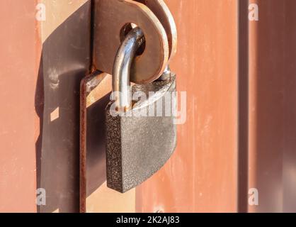 Nahaufnahme-Vorhängeschloss am Tor eines braunen Metallzauns aus modernem Abstellgleis, dem Konzept der Sicherheit. Stockfoto