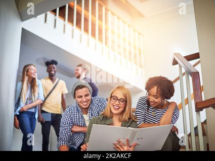 Setzen Sie die Arbeit ein, um ihre Aufgaben zu erledigen. Aufnahme einer Gruppe von Studenten, die auf der Treppe auf dem Campus zusammenarbeiten. Stockfoto