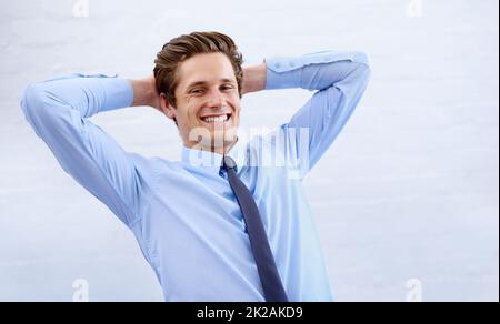 Zufrieden mit seinem Erfolg. Ein zufriedener junger Geschäftsmann, der sich mit den Händen hinter dem Kopf zurücklehnt. Stockfoto