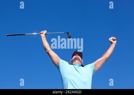 Loch in einem. Low-Angle-Aufnahme eines reifen männlichen Golfers mit erhobenen Armen zur Feier. Stockfoto