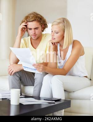 Woher kommen all diese Rechnungen? Ein junges Paar, das zusammen in der Lounge einen Finanzbericht liest. Stockfoto