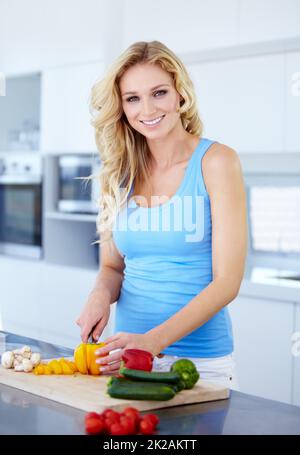 Die gesunde Wahl treffen. Porträt einer hübschen jungen Frau, die in der Küche frische Produkte zerschneidet. Stockfoto