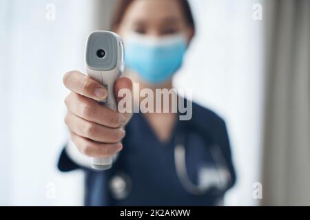 Temperaturkontrollen sind während dieser Pandemie wichtig. Aufnahme einer jungen Ärztin, die auf ein Thermometer in ein Büro zeigt. Stockfoto