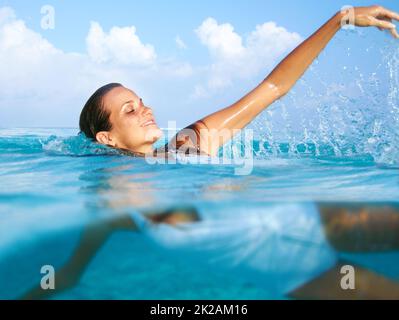 Hochgefühl im Meer. Aufnahme einer schönen jungen Frau, die im blauen Ozean schwimmend ist. Stockfoto