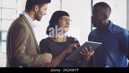 Wir haben darüber gesprochen Eine kurze Aufnahme einer Gruppe junger Designer, die sich in ihrem Büro ein digitales Tablet angeschaut haben. Stockfoto