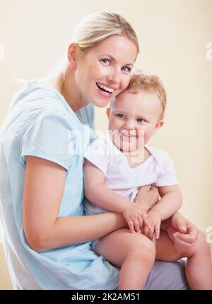 Porträt der Mutterschaft. Ein Porträt einer lächelnden Mutter, die mit ihrem Kind auf ihrem Schoß sitzt. Stockfoto