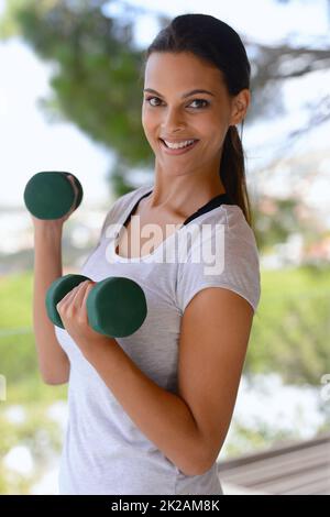 Frische Luft und ein tolles Workout. Porträt einer schönen Frau, die Hanteln an einem Fenster hebt. Stockfoto