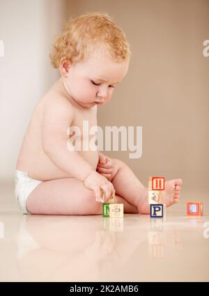 Lernen durch Interaktionen. Niedliches kleines Baby, das auf dem Boden sitzt und mit einigen Alphabet-Blöcken spielt. Stockfoto