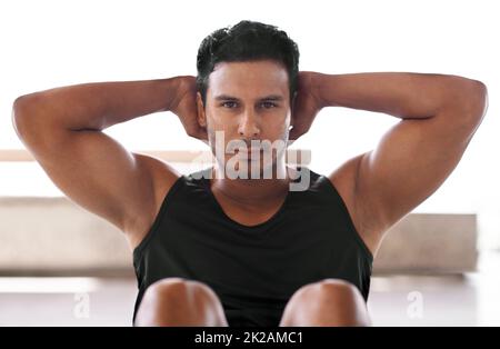 Der Schlüssel zur Fitness ist die Konzentration. Porträt eines fokussierten Mannes, der zu Hause Sit-ups macht. Stockfoto