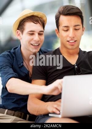 Das ist das perfekte Reiseziel für den Sommerurlaub. Aufnahme eines jungen Mannes, der auf den Laptop seiner Freunde zeigt. Stockfoto