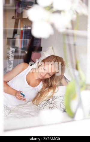 Entspannen Sie sich bei tollen Melodien. Junge Frau liegt im Bett und hört ihrem mp3 Spieler zu. Stockfoto