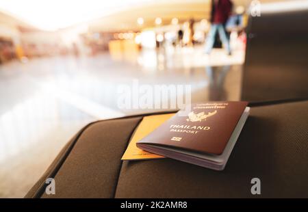 Thailändischer Reisepass und Impfpass auf Gepäck auf verschwommenem Hintergrund von Touristen im Flughafen. Impfzertifikat für Reisen während des Coronavirus-Ausbruchs. Reisedokument nach Covid-19. Stockfoto