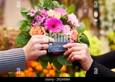 Beweisen, dass Sie Schönheit kaufen können. Kurzer Schuss einer Frau, die Blumen mit ihrer Kreditkarte von einem Floristen kauft. Stockfoto