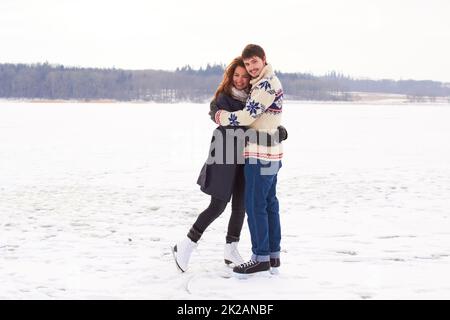 Romantik im Winter. Ein junges Paar auf einem Eislauftermin an einem gefrorenen Natursee. Stockfoto