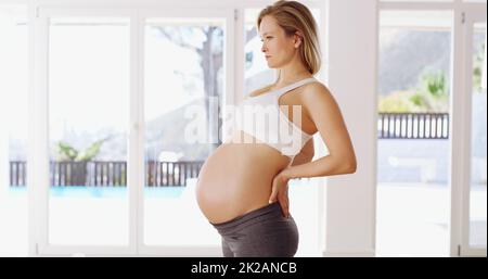 Ihr Rücken nimmt während der Schwangerschaft eine Menge Belastung auf. Das verkürzte Porträt einer attraktiven jungen Schwangeren, die mit den Händen auf dem Rücken steht. Stockfoto