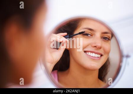 Frau, die Mascara anwendet. Spiegelung einer schönen Frau, die Mascara anwendet. Stockfoto