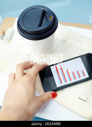 Arbeiten außerhalb des Büros. Smartphone mit Bar-Chart auf dem Bildschirm mit Einweg-Tasse, Stift, Zeitung und Clipboard. Stockfoto