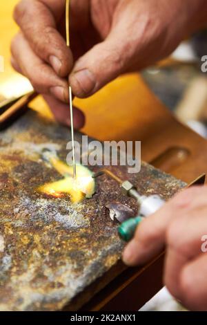 Bei diesem Prozess ist eine sorgfältige Konzentration von entscheidender Bedeutung. Beschnittene Ansicht eines Juwelierherstellers, der Lot aufheizt und einen Lötpick verwendet. Stockfoto