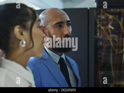 Die Endkontrolle. Aufnahme von zwei jungen Arbeitern, die bei der Arbeit in einem Serverraum Wartungsarbeiten durchführen. Stockfoto