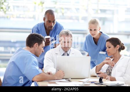 Engagiertes Team von medizinischen Fachkräften. Ein Team von medizinischem Fachpersonal, das um einen Laptop herum arbeitet. Stockfoto