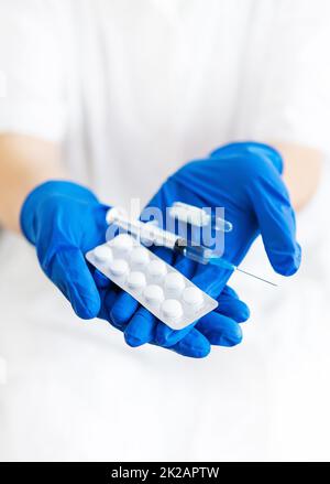 Ein junger Arzt hält einen Impfstoff, eine Spritze und Pillen in latexblauen Handschuhen. Hausarzt macht Impfung. Eine Frau in einer Arztpraxis. Impfungen gegen Influenza und Viren. Stockfoto