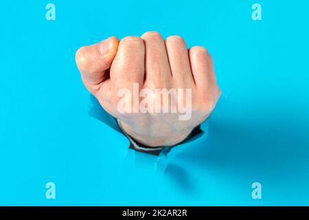 Mann bricht mit der Faust durch blaues Papier Stockfoto