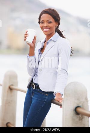 Genießen Sie einen entspannten Spaziergang. Eine wunderschöne afroamerikanische Frau, die Kaffee genießt, während sie spazieren geht. Stockfoto