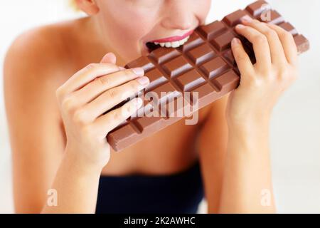 Nichts als sündhafter Genuss. Beschnittene Ansicht einer jungen Frau, die in eine große Schokoladenplatte beißt. Stockfoto