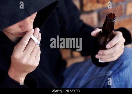 Rücksichtslose Jugend. Topview einer Person, die einen Kapuzenpullover trägt, raucht und eine Flasche Bier hält. Stockfoto