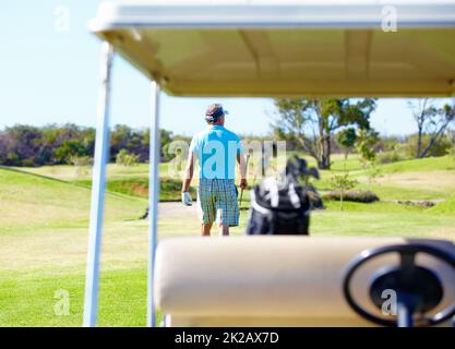 Was für ein toller Tag auf dem Golfplatz zu sein Rückansicht eines Golfspielers, der mit einem Golfwagen im Vordergrund wegläuft. Stockfoto