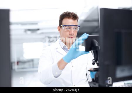 Vornehmen von Anpassungen. Ein Wissenschaftler, der aufmerksam auf ein Mikroskop blickt, während er eine Schutzbrille trägt. Stockfoto
