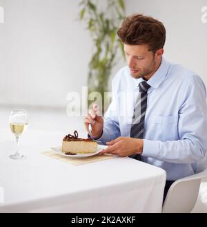 Hes hat einen süßen Zahn. Ein hübscher junger Mann, der in einem Restaurant in ein köstliches Stück Käsekuchen stopft. Stockfoto