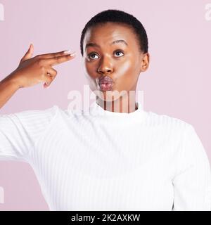 Das Leben ist zu kurz, um nicht sonderbar zu sein. Studioaufnahme einer jungen Frau, die eine Fingergewehrgeste vor einem rosa Hintergrund hochhält. Stockfoto