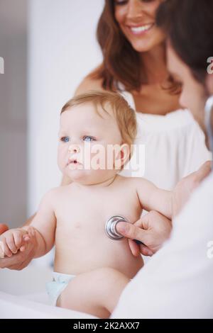 Keine Tränen heute. Eine Mutter, die als ihre kleine Tochter dabeisteht, wird von einem Kinderarzt untersucht. Stockfoto