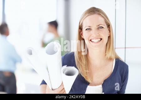 Sie strahlt Vertrauen in sich und ihre Arbeit aus. Porträt einer jungen Architektin, die ihre Entwürfe in der Hand hält. Stockfoto