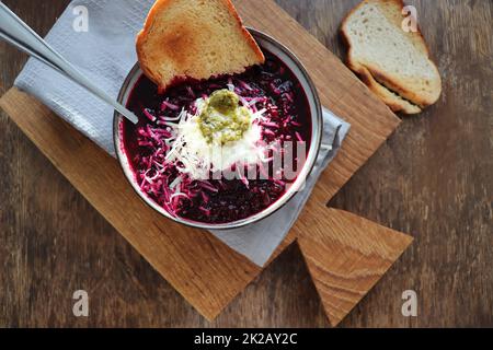 Rote Beete-Sahnesuppe in einer Schüssel mit Käse, Sauerrahm und Brot auf rustikalem Holzhintergrund. Draufsicht, flach liegend Stockfoto